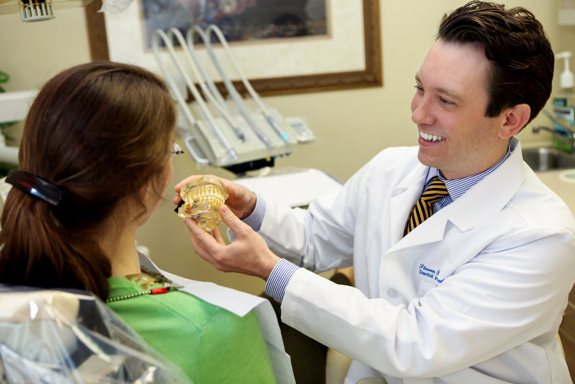 Dr. Swierkowski explaining dental procedures to a female patient using a clear anatomical teeth model during a consultation in the treatment room.